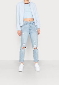 Světle modrá bomber bunda, střihový crop top, zvonové světle modré džíny s výplněmi a bílé tenisky. Neformální, uvolněný střih a design.