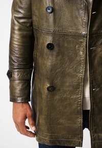 Olive green leather coat with a textured finish, double-breasted design, black buttons, and visible stitching accents.