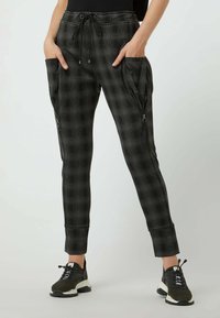 Svart- och grårutig joggingbyxor med elastisk midja, dragsko, sidofickor med dragkedja och smalnande muddar. Materialet verkar mjukt och texturerat.