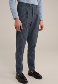 Pantalones de tela azul oscuro con rayas blancas verticales, con un diseño de frente plano, bolsillos laterales y cierre de botón. Terminados con un corte ajustado.