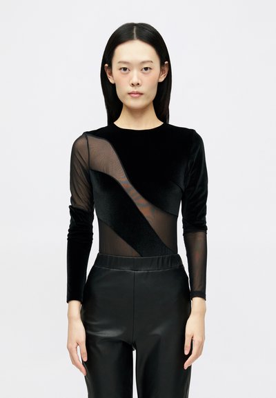 Body negro que cuenta con mangas largas de malla y un frente de terciopelo con un diseño geométrico, combinado con pantalones de cuero negro de cintura alta.