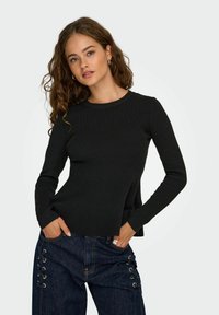 Haut noir à fines rayures à manches longues avec un col rond. Associé à un jean en denim foncé avec des détails à lacets sur le côté et des poches avant.