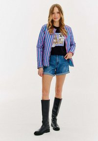 Pasek w kolorze fioletowym i różowym, grafika na czarnej koszulce, szorty dżinsowe i czarne bootsy do kolan. Gładkie tekstury, swobodny krój.