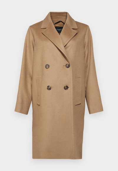 Manteau beige croisé en mélange de laine doux, avec des revers crantés, deux poches avant et de grands boutons foncés.