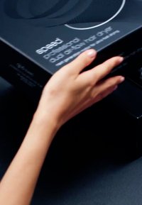 Main tenant une boîte noire étiquetée « séchoir professionnel quad angle vitesse » sur un fond sombre.