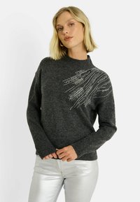 Pull gris foncé en tricot avec un col montant et des manches longues, orné de décorations argentées en motif ondulé sur un côté.