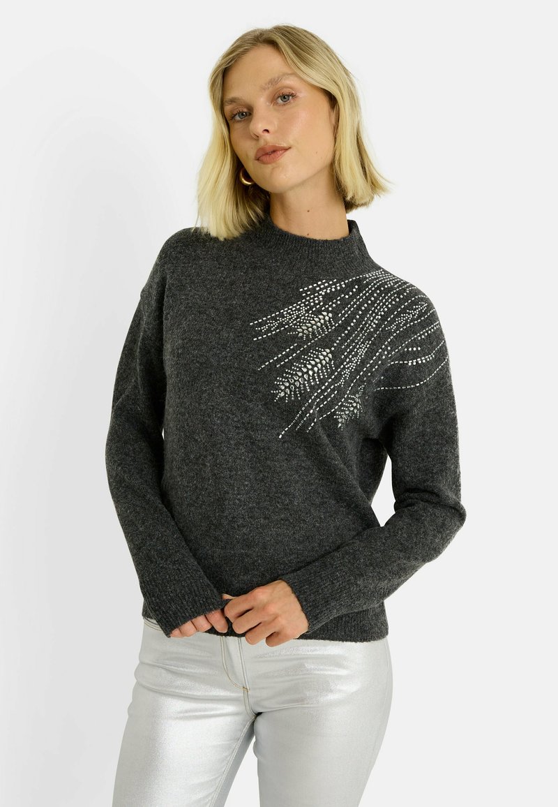 Pull gris foncé en tricot avec un col montant et des manches longues, orné de décorations argentées en motif ondulé sur un côté.