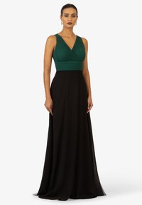 Langes Abendkleid mit einem gefalteten, smaragdgrünen Oberteil und einem fließenden schwarzen Rock. Das Kleid hat einen tiefen V-Ausschnitt und ist ärmellos.