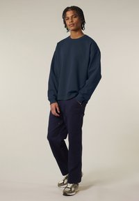 Maglione navy a collo rotondo e maniche lunghe, abbinato a pantaloni blu scuro con tasche, indossato con sneaker grigie e bianche.