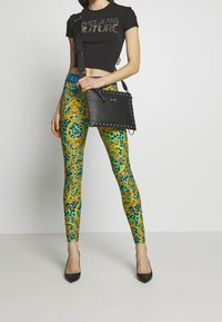 T-shirt nera corta con testo metallico; leggings a fantasia colorati in verde, giallo e blu; borsa nera con borchie; décolleté nere.