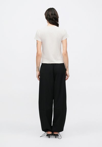 Vaaleanbeige lyhythihainen paita yhdistettynä väljään mustaan housuun. Housuissa on teksturoitu kangas ja nyöritys lahkeissa.