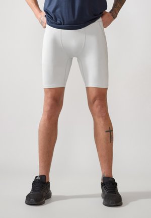 Vita atletiska shorts med en figursydd design, slät ytstruktur, medellängd och hög elasticitet. Bärs med svarta träningsskor.