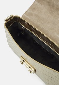 Sac à main en cuir doré avec une texture crocodile, doté d'un fermoir magnétique et d'une douce doublure en daim beige. Poche zip intérieure visible.