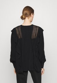 Blusa nera con dettagli arricciati, tessuto testurizzato e sezioni di pizzo trasparente sulla schiena. Presenta un collo rotondo e maniche lunghe a palloncino.