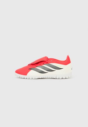 Red and white Adidas Predator turf soccer shoe with black stripes and velcro lace cover, side view on plain background.