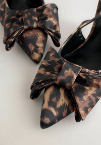Scarpe con tacco alto a punta in tessuto leopardato nero e marrone, con un grande fiocco decorativo sulla parte anteriore. Texture liscia.