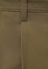 Pantalones verde oliva con una textura de canalé diagonal, cierre de botón y un lazo para cinturón estrecho en la cintura.
