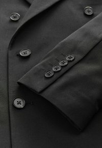 Blazer negro con una textura suave, que presenta seis cierres de botones en el frente y cuatro botones en el puño, todos en negro a juego.