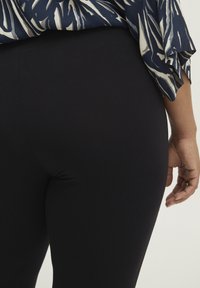 Leggings neri realizzati in tessuto elastico, con una texture liscia e un design aderente, abbinati a un top a motivo in blu navy e crema.