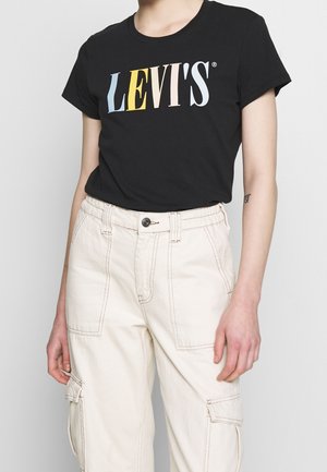 Osoba nosząca czarny t-shirt Levi's z wielokolorowym logo oraz kremowe spodnie cargo z wysokim stanem, z dużymi przednimi kieszeniami i zapięciem na guziki.