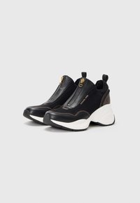 Sneaker neri slip-on con design testurizzato, dettagli in oro con cerniere, suole bianche e dettagli marroni in contrasto. La parte superiore è realizzata in materiale a rete.