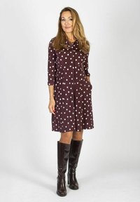 Brązowa sukienka do kolan w białe kropki, z przodem na guziki i długimi rękawami. Posiada boczne kieszenie oraz lekko rozkloszowany dół.