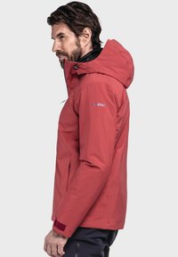 Rote wasserfeste Jacke mit Kapuze, ausgestattet mit einem Reißverschluss, verstellbaren Bündchen und Logodetail am Oberarm. Glattes, langlebiges Material.