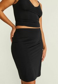 Svart crop top med V-ringning och en åtsittande svart midikjol. Båda tillverkade av ett mjukt, stretchigt tyg och har en elegant, minimalistisk design.
