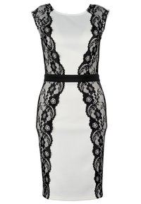 Robe blanche ajustée sans manches avec des panneaux en dentelle florale noire sur les côtés avant et une ceinture noire.