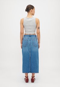 Szürke rövidített tank top, amelyhez egy hosszú kék farmer szoknya párosul, hátsó zsebekkel és egyenes siluettel. Barna boka csizmák egészítik ki a megjelenést.