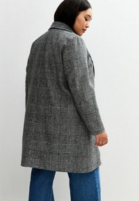 Cappotto grigio a quadri con colletto, maniche lunghe e vestibilità comoda. Il tessuto presenta un motivo testurizzato, abbinato a pantaloni in denim blu.