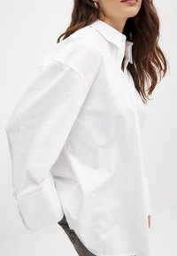 Witte katoenen shirt met een klassieke kraag, oversized mouwen en knoopmanchetten. Gladde textuur met een losse pasvorm en een minimalistisch design.