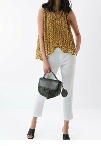 Žlutý top bez rukávů s černými puntíky, bílé kalhoty a zelená kabelka s texturovanou klopou a třásňovým detailem. Černé nazouváky.