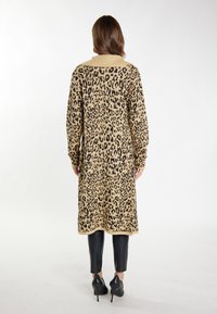 Leopardenmuster-Cardigan in Beige und Schwarz, langärmlig, mit einem gerippten Kragen und strukturiertem Strick, kombiniert mit schwarzen, figurbetonten Hosen und High Heels.