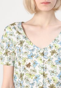 Top a maniche corte con scollo a V, decorato con un motivo floreale blu, verde e marrone su uno sfondo chiaro, con dettagli in bottone sul fronte.