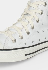 Λευκό πάνινο sneaker με λευκά κορδόνια, μεταλλικές οπές, ασημί πουα σχέδιο και λευκή καουτσούκ σόλα με μαύρες ρίγες.