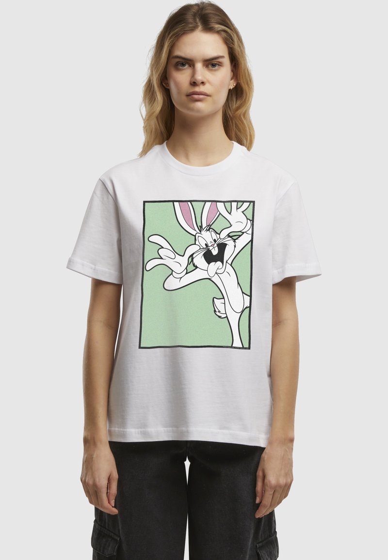 T-shirt en coton blanc avec un graphique de lapin en cartoon noir et rose sur un fond vert, à l'intérieur d'un contour noir. Manches courtes.