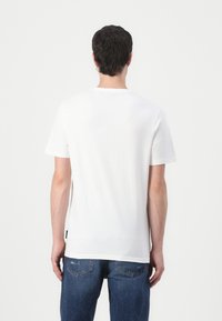 Tricou alb din bumbac, cu mâneci scurte, guler rotund și fante laterale. Purtați cu blugi din denim albastru cu o ușoară decolorare.