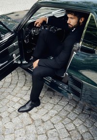 Klasyczne wnętrze czarnego sportowego samochodu z skórzaną fotelem i chromowanymi akcentami. Mężczyzna w czarnym garniturze siedzi na miejscu kierowcy.