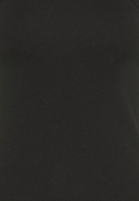 Gros plan sur un tissu noir montrant une texture lisse avec un léger détail de couture dans le coin supérieur droit.