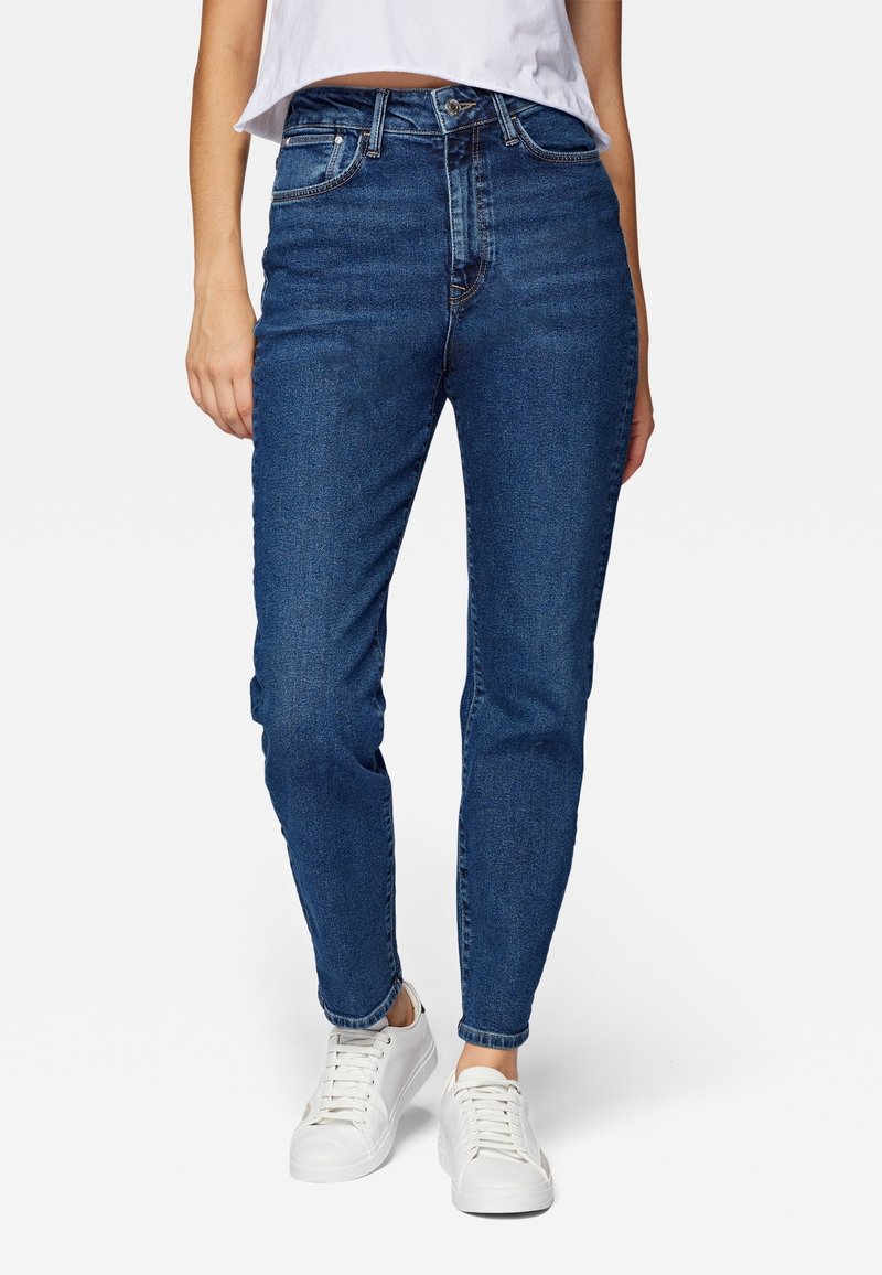 Jean bleu taille haute à coupe slim, cinq poches, délavage subtil et détails de couture, assorti à des baskets blanches.