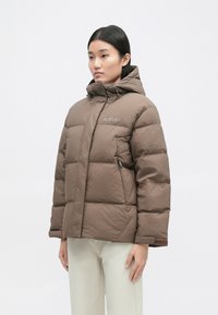 Pruun puffer-jakk kapuutsiga, millel on tikanditud disain, lukuga taskud ja logo rinnal. Sile, veekindel materjal.