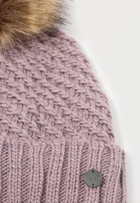 Pletená čiapka v jemnej levandulovej farbe, s textúrovaným kablovým vzorom, rebrovaným okrajom a umelým kožušinovým pom-pom na vrchu. Obsahuje aj kovový detail loga.
