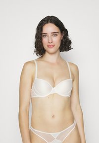 Helle beige BH mit gepolsterten Cups und Spitzenverzierungen an den Seiten. Verstellbare dünne Träger und eine glatte Textur erhöhen den Komfort und die Passform.