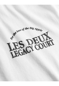 Bílá tkanina s texturou a černým potiskem textu: "Pro lásku k Velkému jablku" a "LES DEUX LEGACY COURT."