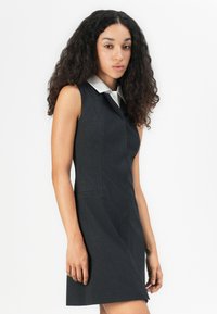 Mustaton, ilman hihoja oleva raidallinen mekko valkoisella kauluksella, joka on slim fit -mallinen ja jossa on sivutaskut.