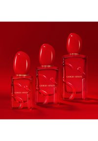 Tres botellas de perfume Giorgio Armani rojas con tapones rojos curvos dispuestas por tamaño contra un fondo rojo.