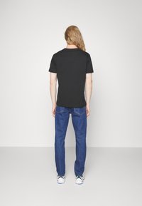 Černé tričko s krátkým rukávem v kombinaci s modrými džínami. Materiál je hladký a střih je pravidelný. Boty jsou černé, bílé a modré barvy.