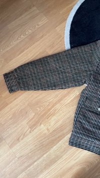 Manche de pull en maille à carreaux en vert foncé, rouge et blanc. Présente un poignet côtelé et un tissu texturé avec un motif diagonal.