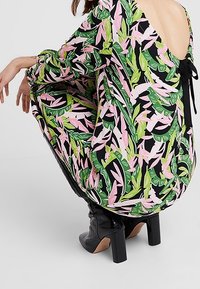 Floral dress with a black base, featuring green and pink leaf patterns; scoop back with tie detail; fabric appears lightweight and flowy.